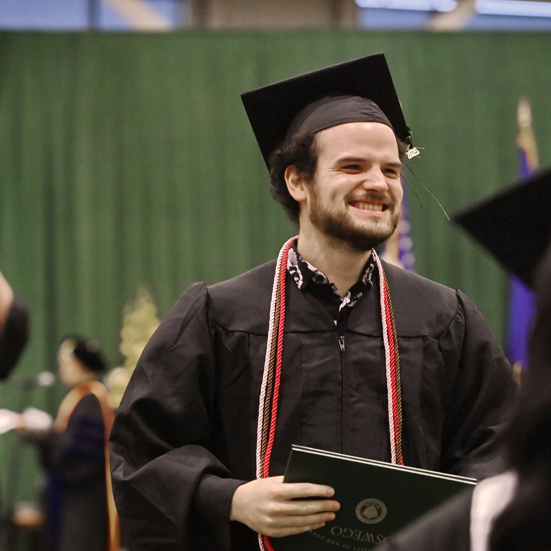 Joshua Phelan smiling in his cap and gown at SUNY Oswego graduation